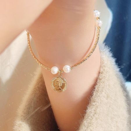 Detailed view of the 14K gold-plated bracelet showcasing the pearl and coin charm.