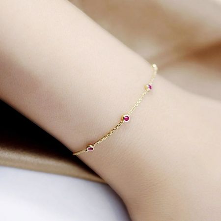 Un delicato bracciale in argento sterling 925 con finitura dorata e un ciondolo rotondo in pietra preziosa rossa, esposto su uno sfondo neutro.