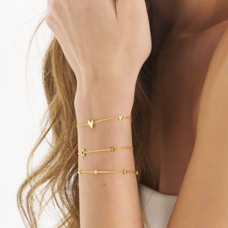 A collection of gold charm bracelets, including the heart link design, styled on a wrist.