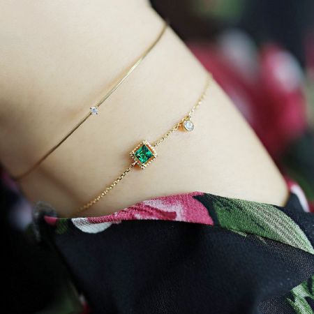 A set of two matching gold-plated bracelets with green and clear zircon stones.