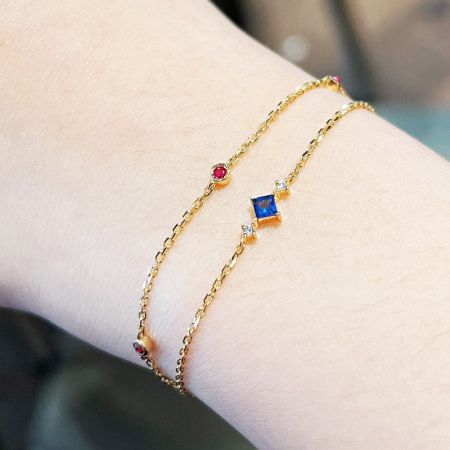 Zwei goldene Edelsteinarmbänder, die an einem Handgelenk getragen werden, um einen geschichteten Look zu demonstrieren.