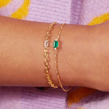 Un modelo que lleva la pulsera de cadena Figaro de oro con una piedra preciosa verde, mostrando su ajuste elegante en la muñeca.