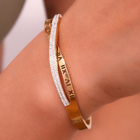 CZ Love Bracelet - Roestvrijstalen gouden Romeinse cijfer bangle set - De pols van een persoon versierd met de elegante CZ Love Bracelet, die de 18K gouden plating en het ingewikkelde ontwerp van de Romeinse cijfers toont.