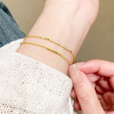Pulseras de Cadena de Diseño de Barra de Zirconia de Doble Capa de Plata Esterlina 925 al por mayor (Juego de 5) - Un primer plano de la muñeca de una mujer adornada con dos elegantes pulseras de cadena de doble capa de plata esterlina 925 con un acabado dorado, que presentan una barra de zirconia brillante.