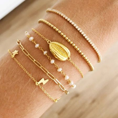 Meerdere gouden armbanden, waaronder de paperclip kettingstijl, gelaagd op een pols.