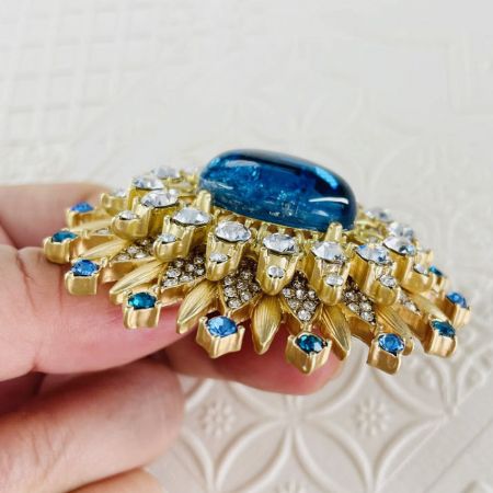 Gedetailleerde opname van de vergulde kristallen zon broche, met focus op het vakmanschap en de zetting van de edelstenen.