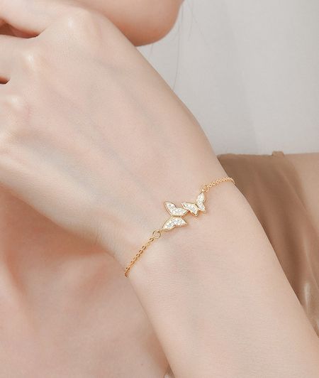 Primer plano de la pulsera de mariposa chapada en oro en una muñeca, destacando su acabado lujoso.
