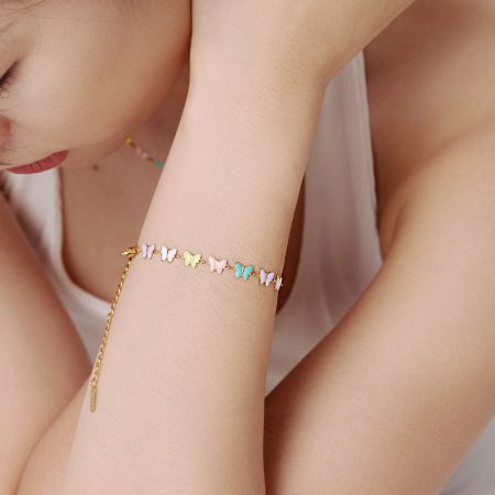 モデルの手首にエレガントに着用された金の蝶のチャームブレスレットが、その鮮やかな色を引き立てています。