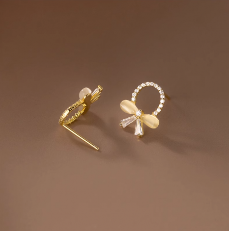 Un paio di orecchini a farfalla in oro con pietre di zirconia chiare e bianche su uno sfondo bianco.