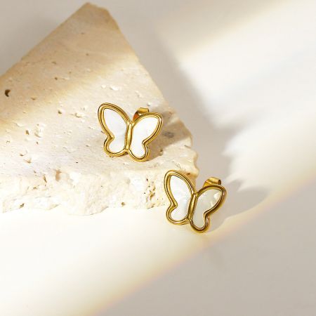 Los pendientes de mariposa de oro con incrustaciones de nácar descansan sobre una superficie de piedra texturizada.