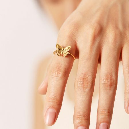 Anelli aperti regolabili in acciaio inossidabile placcati oro a forma di farfalla - Set di 5 - Un primo piano della mano di una donna che indossa un elegante anello a forma di farfalla in acciaio inossidabile placcato oro, mostrando il suo design aperto regolabile.