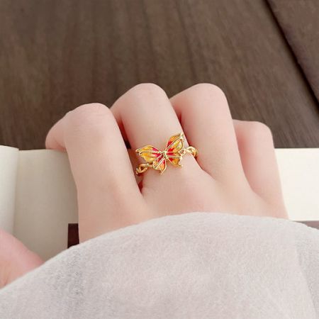 Een delicate vergulde vlinder ring met een verloop van oranje en rode emaille, gedragen op een vinger.