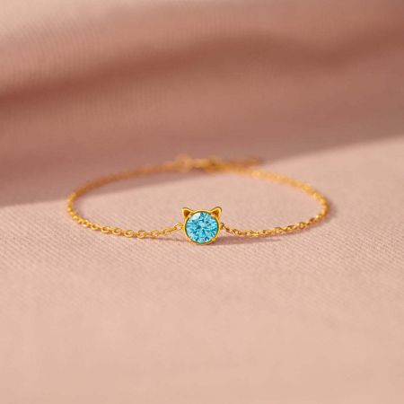 925 Sterling Zilveren Kattenarmband met Blauwe Cubic Zirconia. - Een delicate 925 sterling zilveren kattenarmband in een goudkleur, met een minimalistische kattengezichthanger en een sprankelende blauwe cubic zirconia.