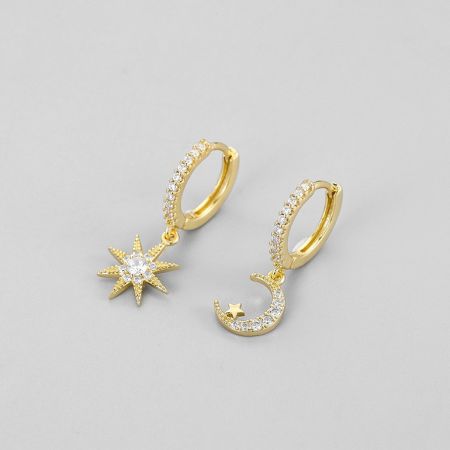 Vista detallada de los pendientes huggie de oro con temática celestial, adornados con charms de estrella y luna.