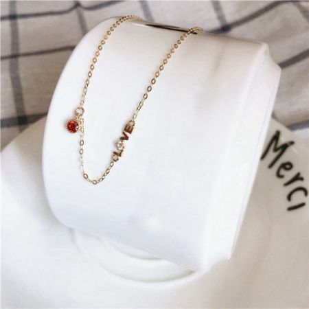 Collar con colgante de amor chapado en oro de 14K de plata esterlina 925 con CZ roja. - Un collar de plata esterlina chapado en oro de 14K que presenta un colgante reversible de 'AMOR' con un circonio cúbico rojo, exhibido en un soporte blanco.