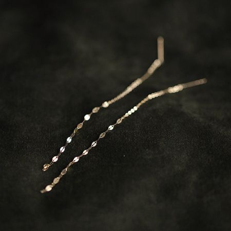 Stijlvolle gouden kettingtassel oorbellen weergegeven op een zwarte achtergrond om hun moderne ontwerp te benadrukken.