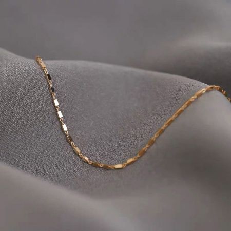 Toma del producto de la delicada pulsera de cadena de geometría cuadrada con acabado dorado sobre un fondo neutro.