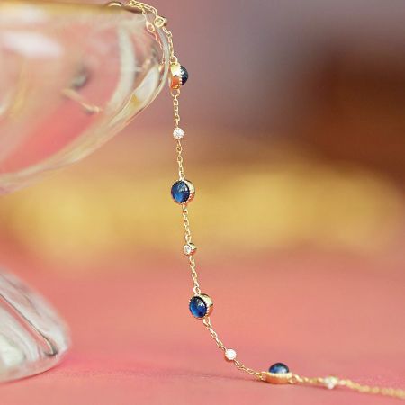 Detaillierte Ansicht eines zarten vergoldeten Kettenarmbands mit abwechselnden blauen und weißen Edelsteinen.