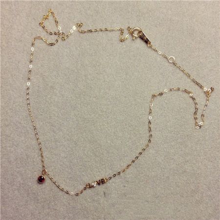 Vista completa del collar de cadena de oro con el llamativo colgante de gema roja en forma de amor.