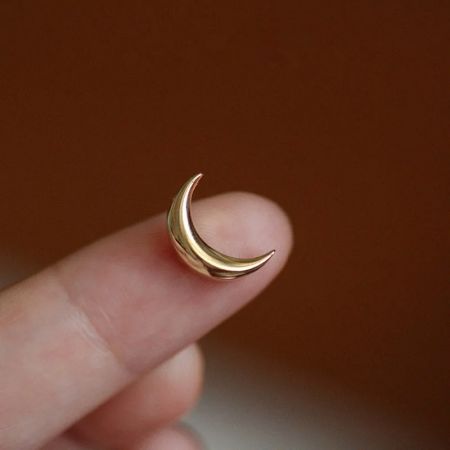 Un orecchino a forma di luna crescente dorata abbinato tenuto per mostrare i dettagli e l'artigianato.
