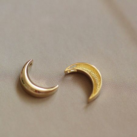 Due pendenti a forma di luna crescente dorata che mostrano lievi variazioni nella texture.