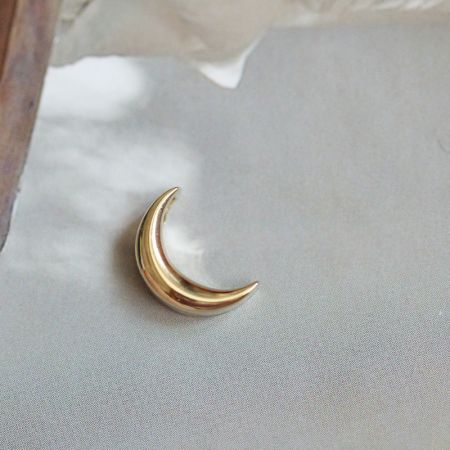 Primo piano del pendente a forma di luna crescente dorata, evidenziando la sua finitura lucida.