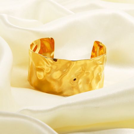 Detaljerad vy av den texturerade, hamrade ytan på det guld rostfria stålarmbandet.