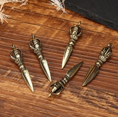 Una collezione di cinque ciondoli strumentali patriarcali esoterici tibetani personalizzati in finitura dorata, esposti su legno.