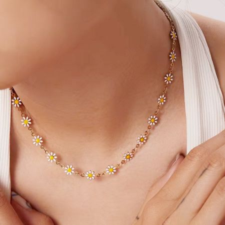 Collares choker de cadena de flor margarita de esmalte de acero inoxidable, set de 5 - Un primer plano de una mujer usando un delicado collar de cadena de oro con encantos de margarita de esmalte blanca y amarilla, mostrando su aspecto elegante.