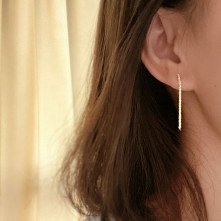 Una modella che indossa l'orecchino pendente dorato in argento sterling 925, evidenziando la sua elegante lunghezza.