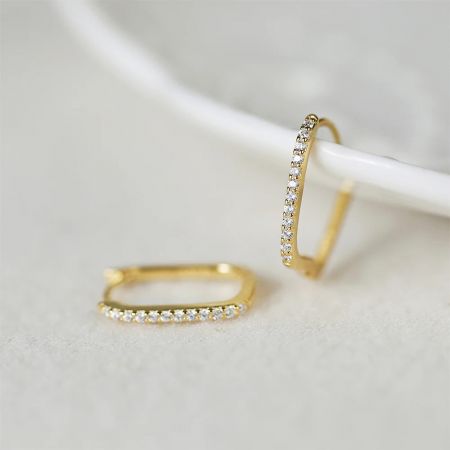 Primo piano dell'orecchino huggie a forma di rettangolo in oro con pietre bianche scintillanti.