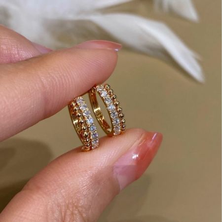 Una mano che tiene due orecchini huggie in argento sterling placcati in oro 18k per mostrare i loro dettagli intricati con perline CZ.
