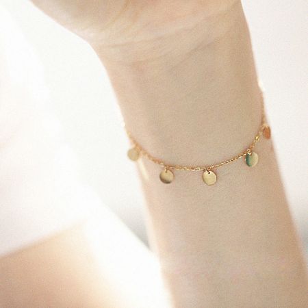 Gedetailleerd uitzicht op een vergulde sterling zilveren armband met kleine schijfcharms.