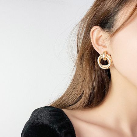 マットゴールドの幾何学的ノットスタッドイヤリングを着用したモデル、サイズとスタイルを披露しています。