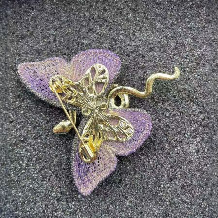 A styled shot of the gold butterfly brooch pinned to a purple fabric flower.