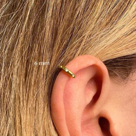 Primo piano di un orecchino a cerchio in oro da 6 mm indossato come piercing al cartilagine.