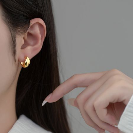 Close-up van een vrouw die een gouden onregelmatige geometrische huggie hoop oorbel draagt.