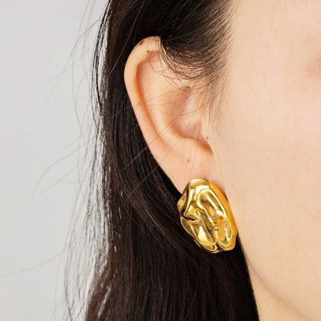 Primer plano de un modelo que lleva los pendientes irregulares de oro martillado.