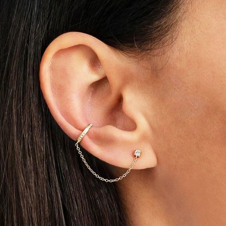 Close-up van de gouden zircon kettinglink oorclip aan een oor.