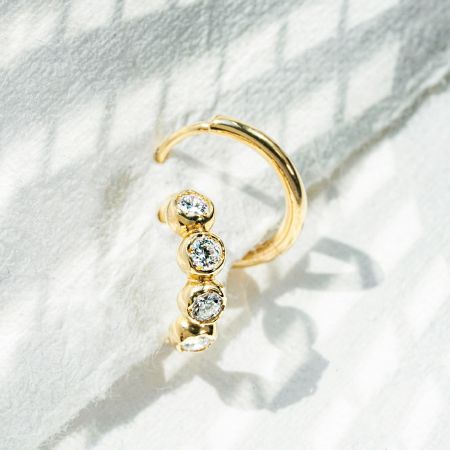 Ett sterlingsilver hoop örhänge med tre klara CZ-stenar på en texturerad vit bakgrund.