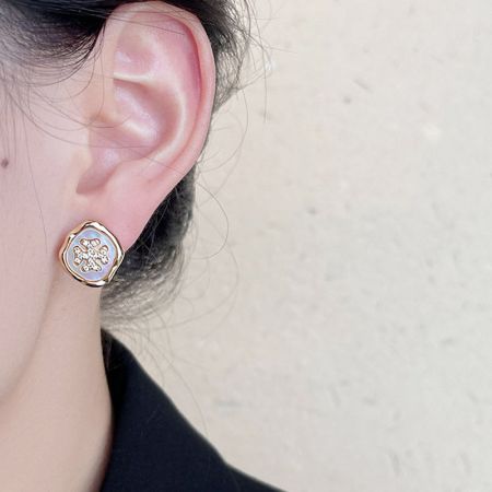 白と金の花柄の単体の金のスタッドピアスの詳細なビュー。