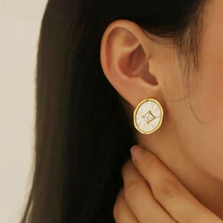 宝石デザインを示す、金と白の樹脂イヤリングの角度を変えたビュー。