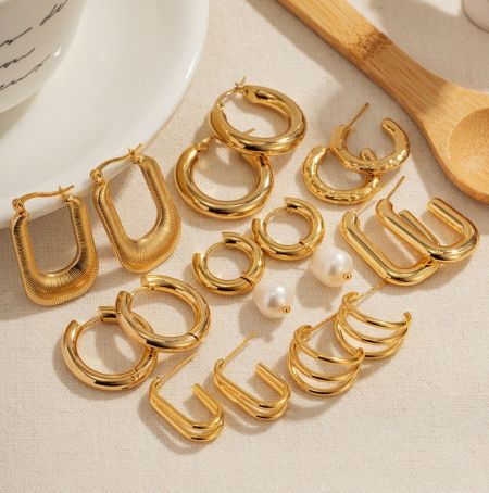 Aretes de aro chapados en oro de 18K de acero inoxidable. - Una colección de aretes de aro chapados en oro de 18K de acero inoxidable, que muestra varios diseños incluyendo aros en forma de U y texturizados, exhibidos sobre un fondo neutro.