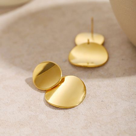Een paar eigentijdse oorbellen van roestvrij staal met gouden afwerking tegen een neutrale achtergrond.