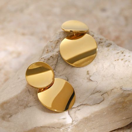 De geometrische ronde schijf oorbellen elegant weergegeven op een gestructureerde beige steen.