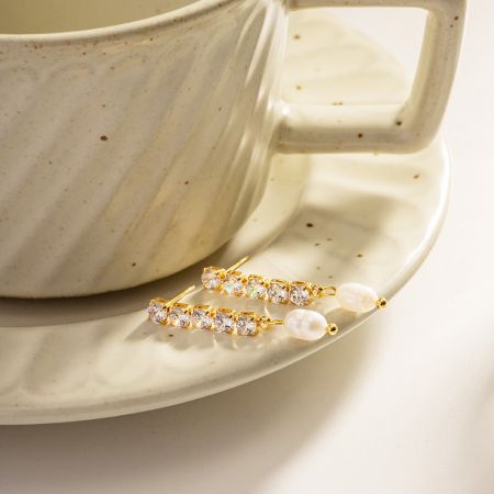 Een lifestylefoto van de delicate parel franje oorbellen die op een wit koffiekopje schotel rusten.