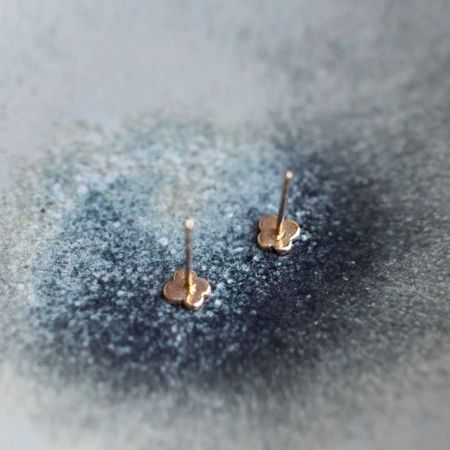 Pendientes de mariposa minimalistas chapados en oro de 14K mostrados sobre un fondo texturizado azul-gris.