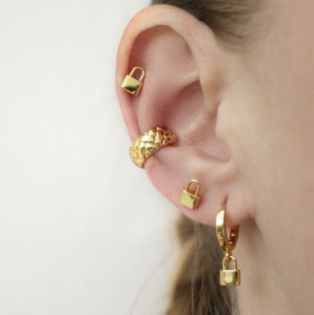 Vue rapprochée des boucles d'oreilles en forme de cadenas doré et des créoles sur une oreille.