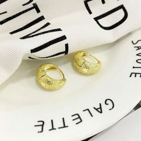 Scatto di lifestyle degli orecchini a cerchio a forma di borsa in oro appoggiati su un piatto di ceramica bianca.