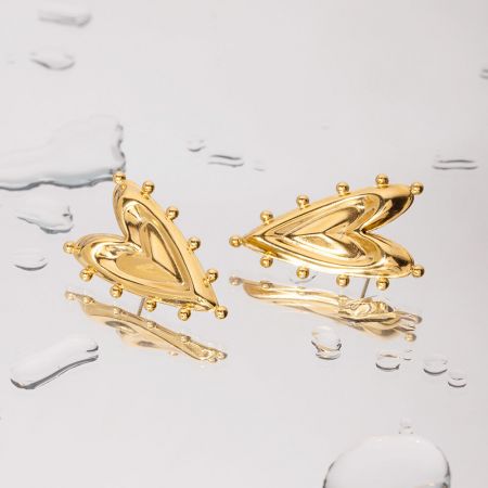 Productfoto van de abstracte gouden hart oorbellen op een witte ondergrond met waterdruppels, die hun reflecterende afwerking benadrukt.